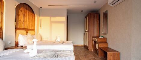 A hotel room with two beds, a wooden wardrobe, a vanity with a mirror, and a hanging light fixture.