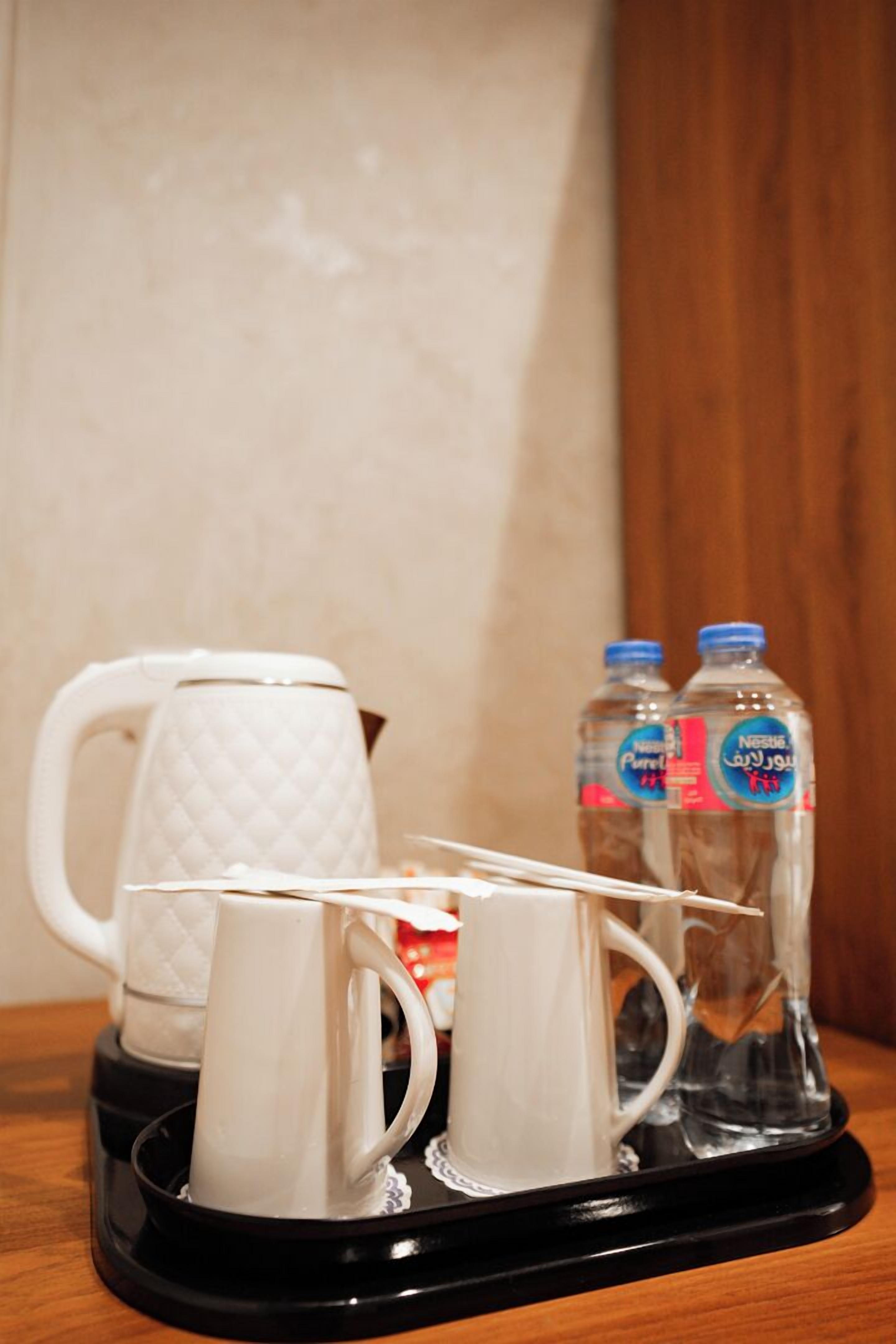 A tray with a white mug, two white cups, and two water bottles on a black tray.