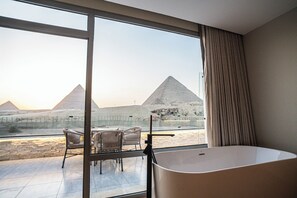 A modern hotel room with a large window offering a view of the pyramids. - Beyond Pyramids Hotel (Giza)