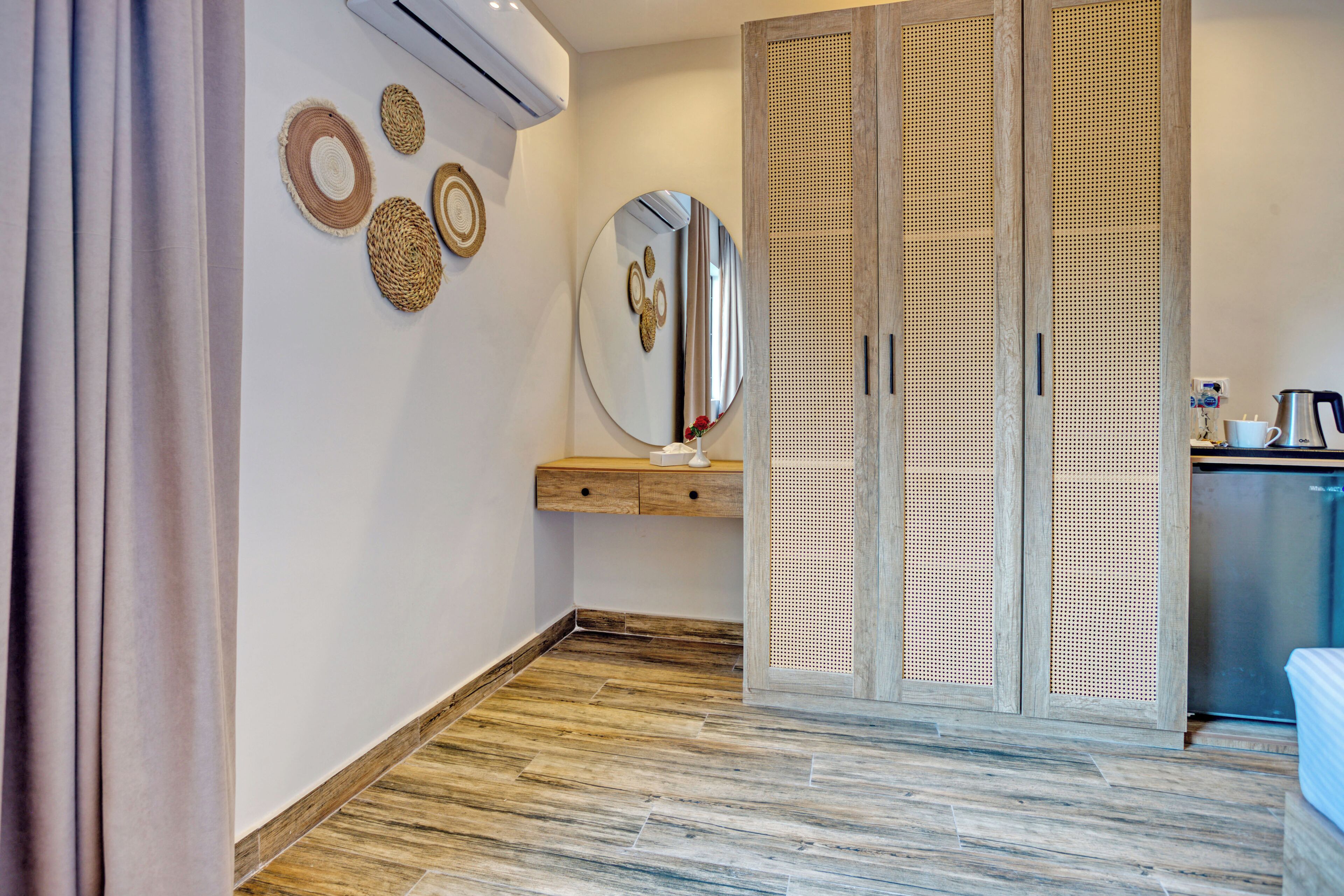 Habitación de hotel con piso de madera, un espejo grande, un armario de madera y un pequeño estante de madera con adornos.