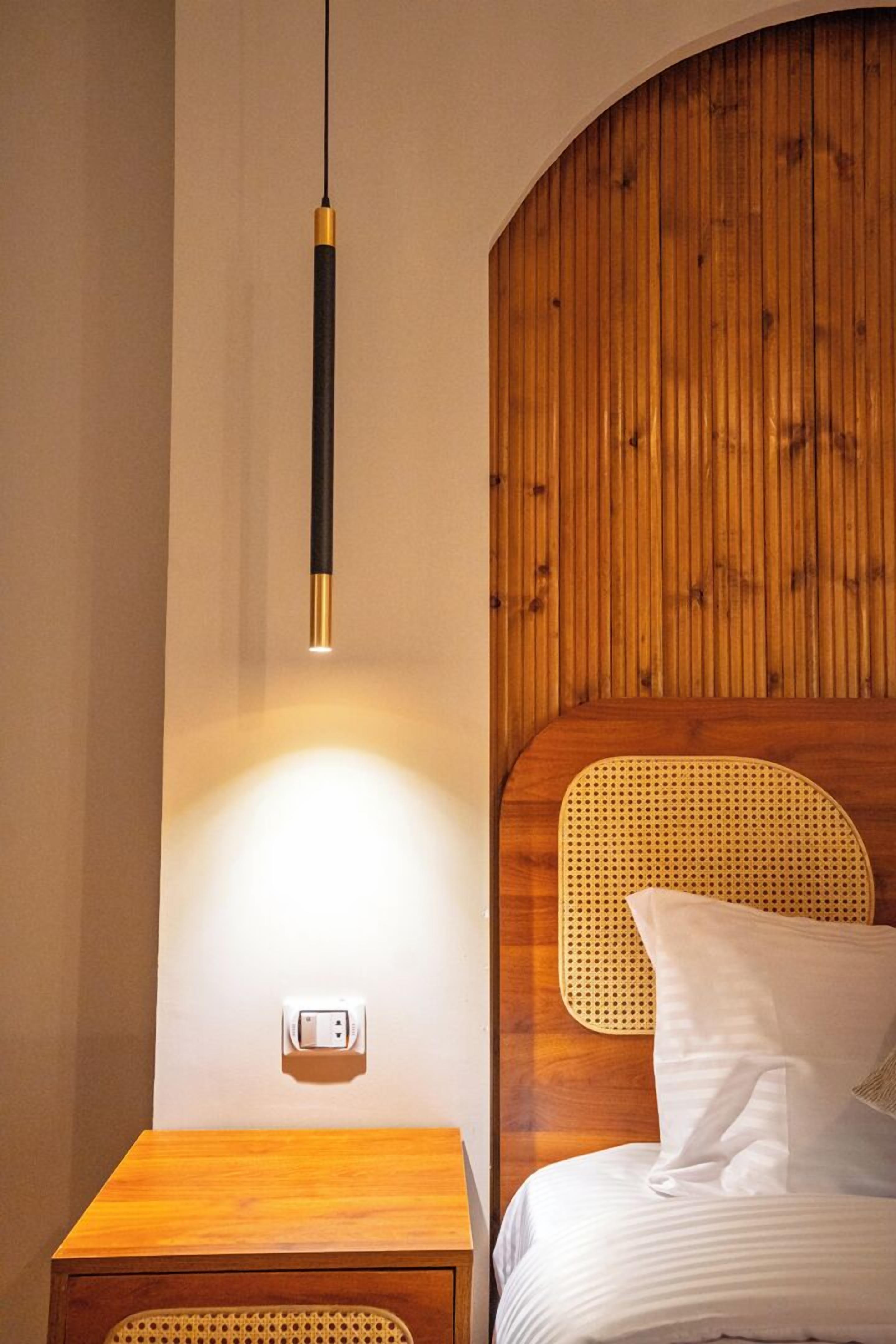 A bedroom with a wooden headboard, a bedside table, a lamp, and a power outlet.