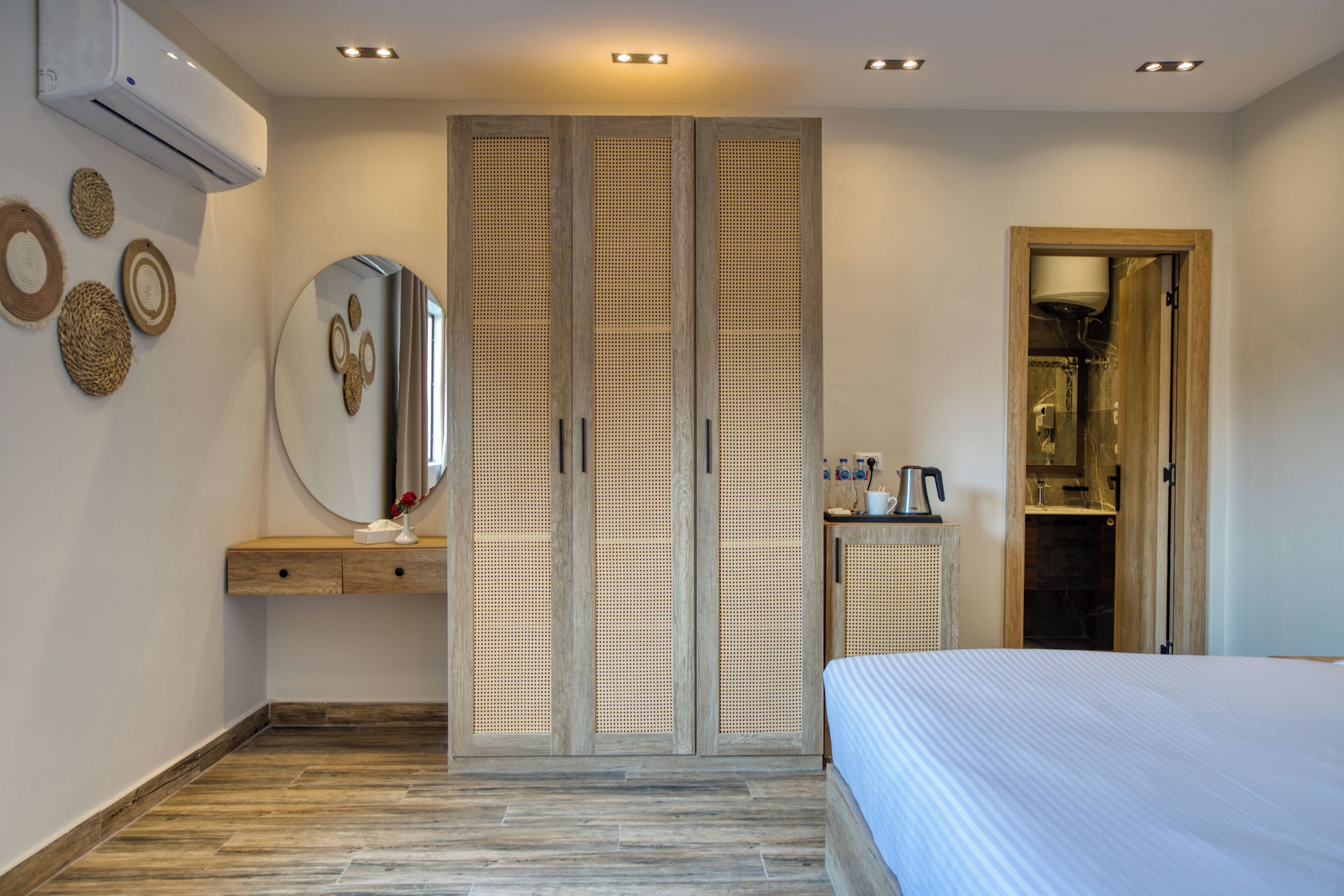 A bedroom with a bed, a wardrobe, a mirror, a small table with a kettle, and a wall-mounted air conditioner.