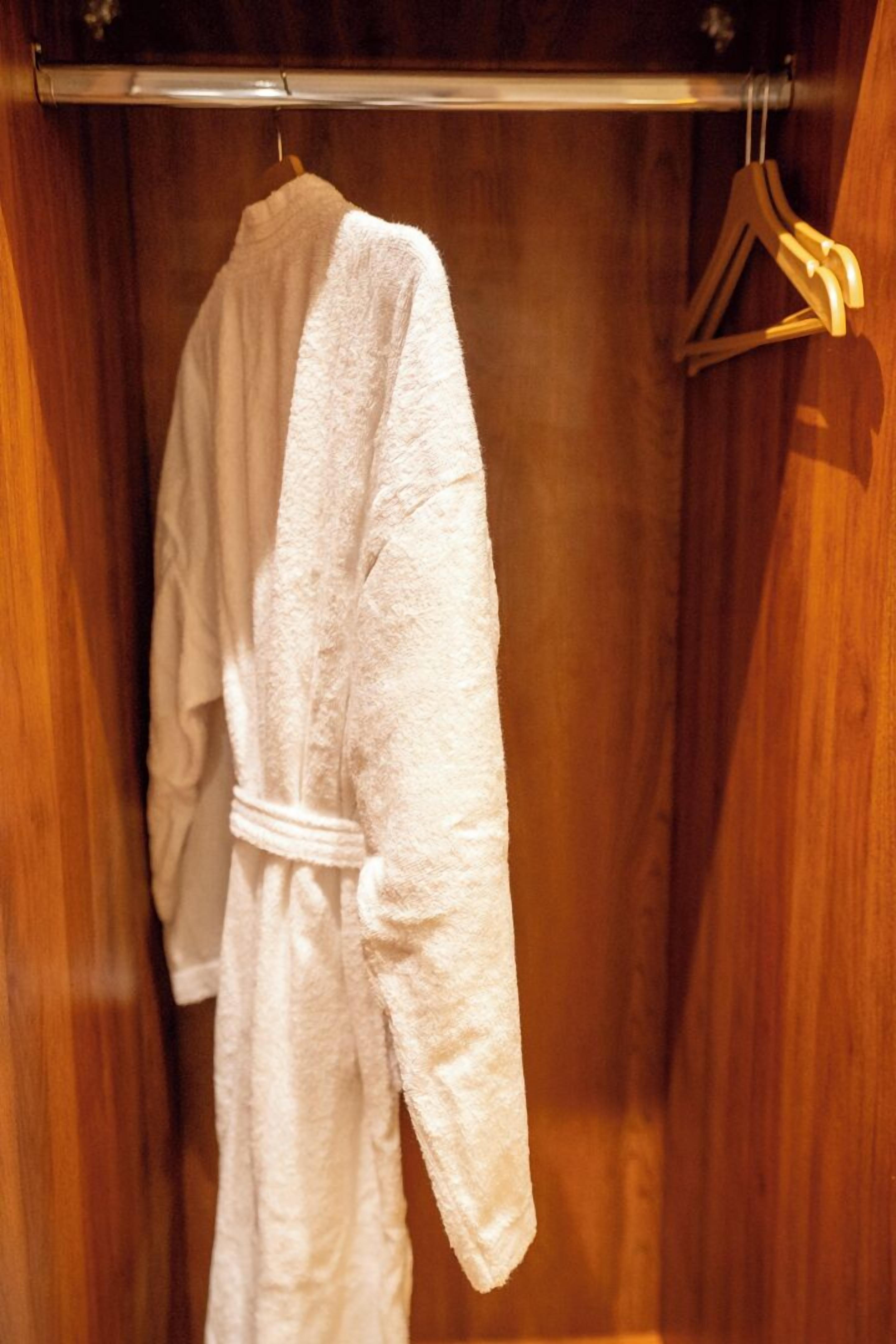 Una bata blanca colgada en una percha de madera dentro de un armario de madera.