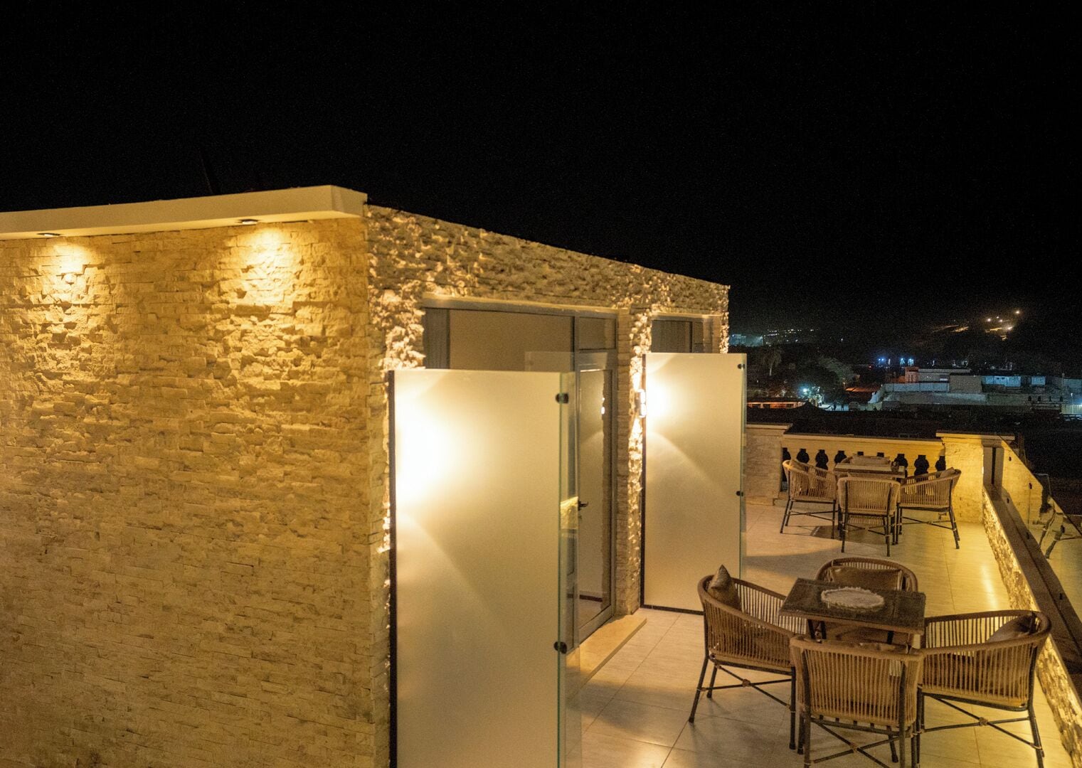 Una terraza en la azotea con muros de piedra, un ventanal y muebles de mimbre.