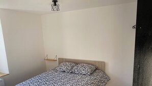 A bedroom with a bed, a hanging light fixture, and a small shelf. - Apartment 2 people -Poncin (Poncin)
