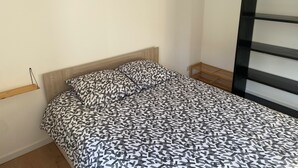 A bedroom with a bed, a wooden headboard, a bedside table, and a wall-mounted shelf. - Apartment 2 people -Poncin (Poncin)