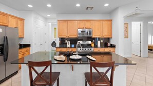 A modern kitchen with wooden cabinets, stainless steel appliances, and a glass island with two chairs. - Family Friendly  w/ Badminton | Goodyear Park (Goodyear)