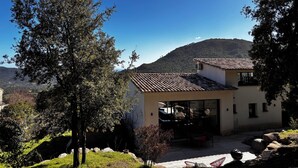 A house with a tiled roof, a patio with outdoor furniture, and a view of a mountain. - Villa located between sea and mountains (Conca)