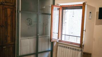 Una stanza con soffitto in legno, un'ampia finestra con cornice in legno, un termosifone sotto la finestra e un letto con asciugamani piegati su un tappeto bianco.