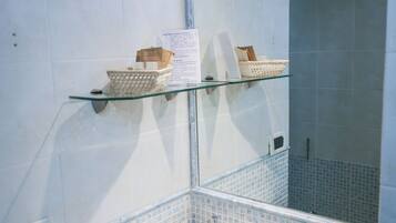 Une salle de bain avec un lavabo blanc, une étagère en verre où sont rangés les articles de toilette, et un miroir au-dessus du lavabo.