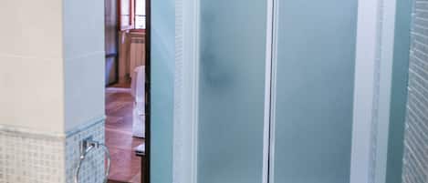 A bathroom with a shower, a sink, and a door leading to another room.