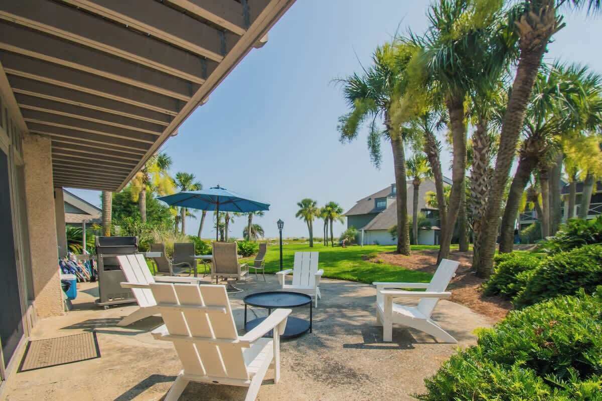 An outdoor seating area with white chairs, a round table, and a blue umbrella.