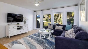 A living room with a TV, white cabinet, sofa, and a glass coffee table. - 332 Capt John Fripp Villa (Fripp Island)