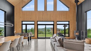 A modern interior with a wooden ceiling, large windows, a sofa, a table, and a fireplace.