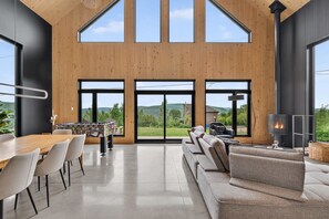 A modern interior with a wooden ceiling, large windows, a sofa, a table, and a fireplace.
