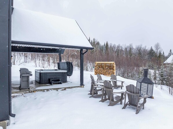 A covered outdoor seating area with Adirondack chairs, a barbecue grill, and a hot tub.