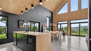 A modern kitchen with a central island, large windows, and a dining area with chairs.