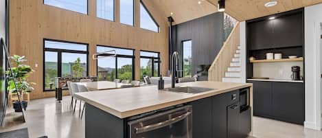 Une cuisine moderne dotée d’un grand îlot central, d’appareils électroménagers intégrés et d’un escalier menant à un niveau supérieur.