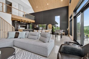 A modern interior with a grey sectional sofa, a dining area, and a kitchen.