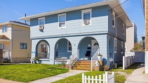 A two-story house with a blue exterior, a front porch with steps, and a white picket fence.