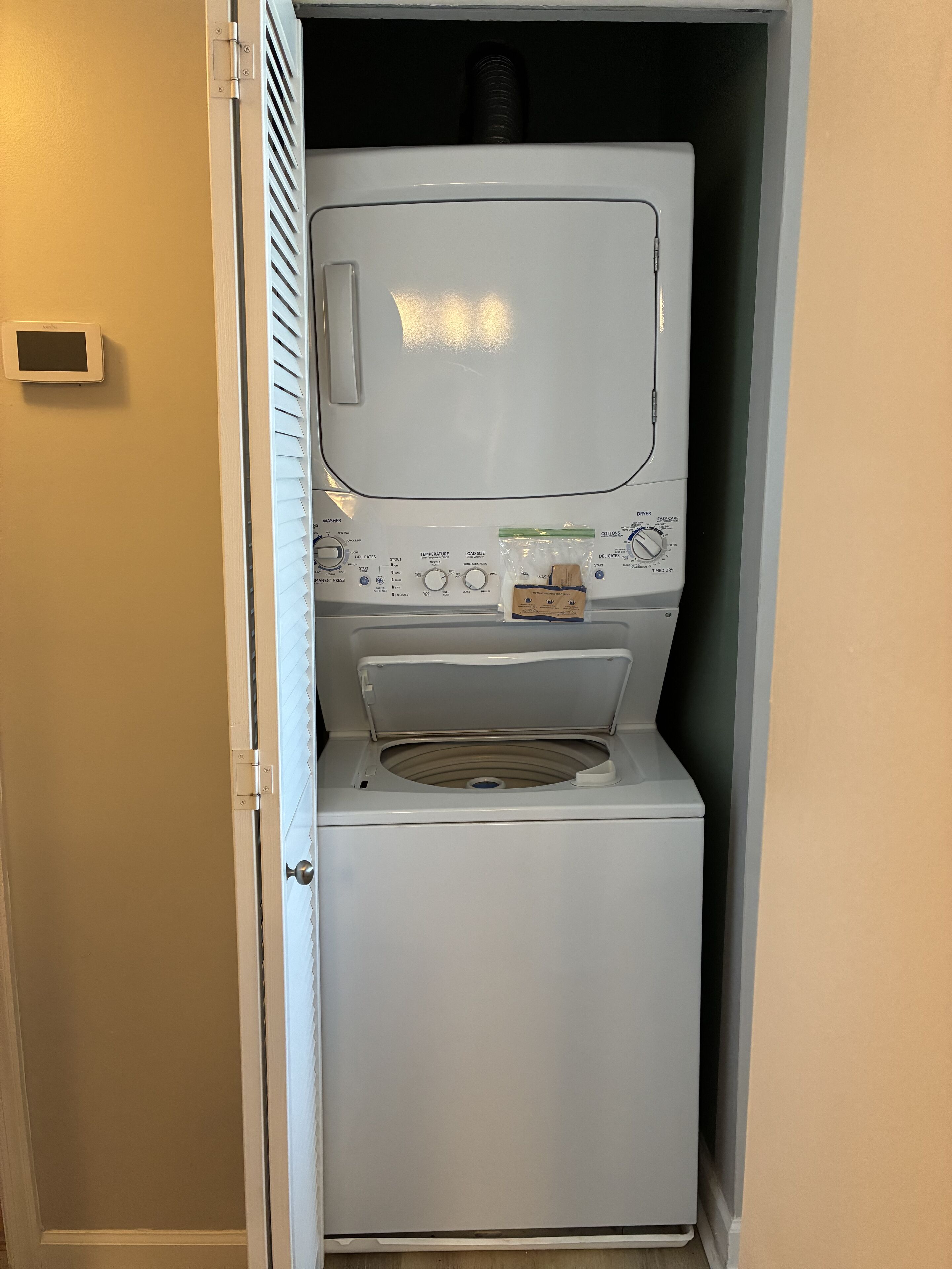 Une machine à laver compacte, de couleur blanche, à chargement frontal, dotée d’un panneau de commande, d’un petit compartiment de rangement et d’une ouverture d’aération sur le dessus.