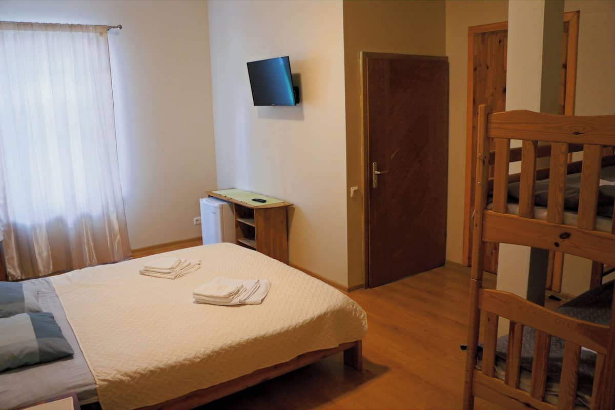 Une chambre à coucher avec un lit, un téléviseur fixé au mur, une porte en bois et une chaise en bois.