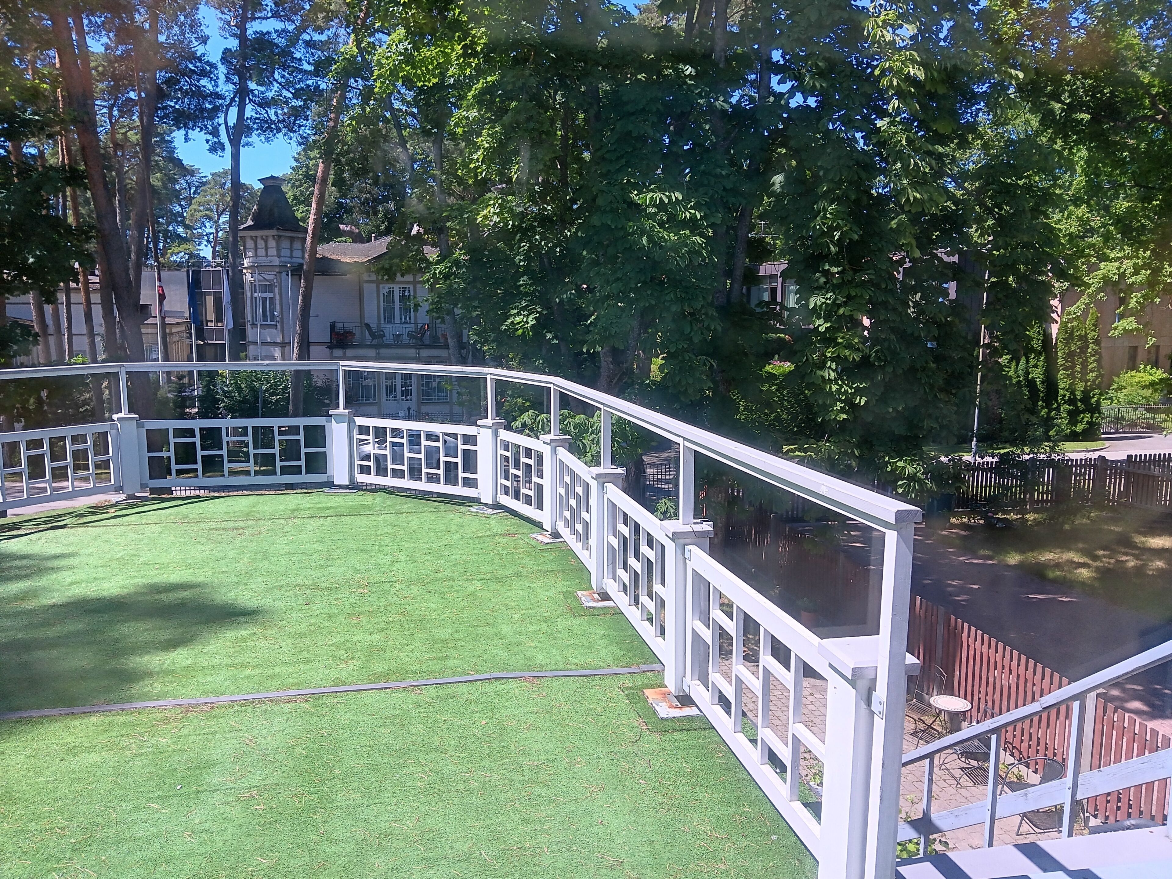A curved white fence surrounding a grassy area with a view of a building and trees.