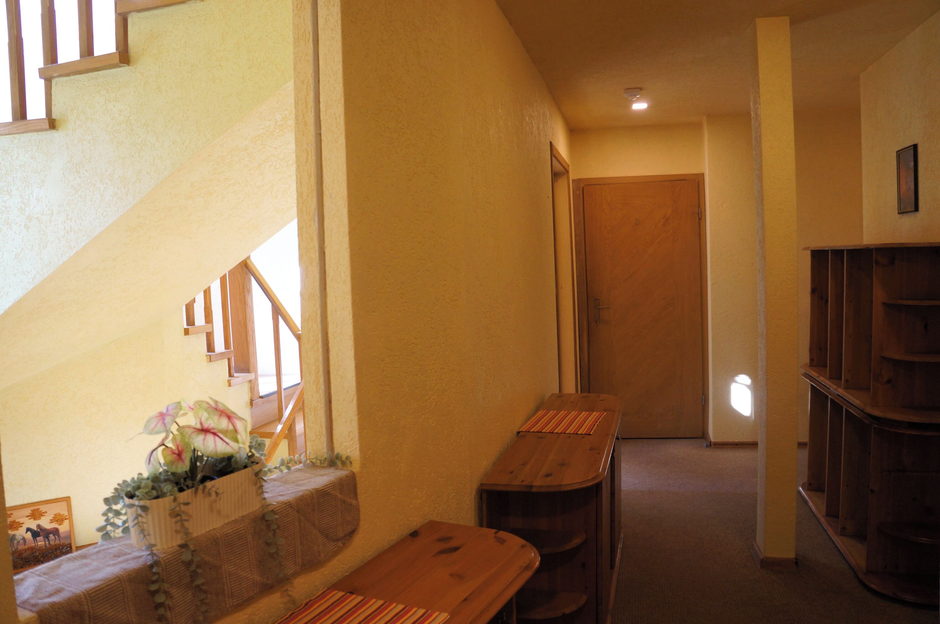 A hallway with a wooden staircase, a wooden door, and a bookshelf.