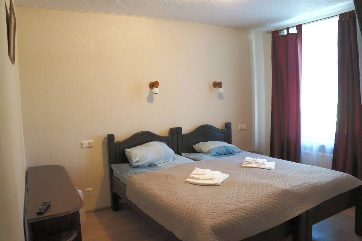 Une chambre d’hôtel avec deux lits, une table de chevet, une télécommande et une fenêtre avec des rideaux.