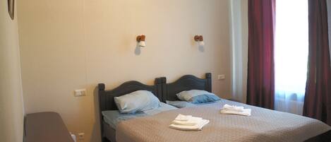 A hotel room with two beds, a bedside table, a remote control, and a window with curtains.