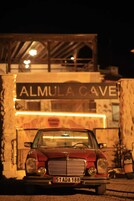 A vintage red car parked in front of a building with a sign reading "ALMULA CAVE".