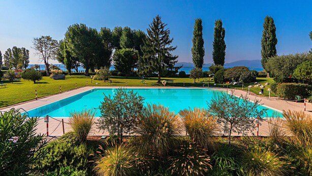 Una piscina rectangular rodeada por una valla, con una vista despejada del cielo y montañas distantes.
