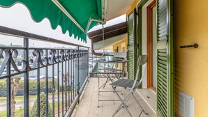 Un balcón con toldo verde, barandilla metálica, una mesa con sillas y vistas a la ciudad.
