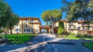 Un edificio residencial con un arco central, un camino de entrada pavimentado y zonas verdes circundantes.