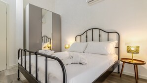 Un dormitorio moderno con una cama de estructura metálica, un espejo grande, lámparas de noche y una mesita de madera.