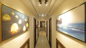 A hallway with artwork on the walls, a wooden floor, and a ceiling with recessed lighting. - Treebo Paarth Grand (Haridwar)