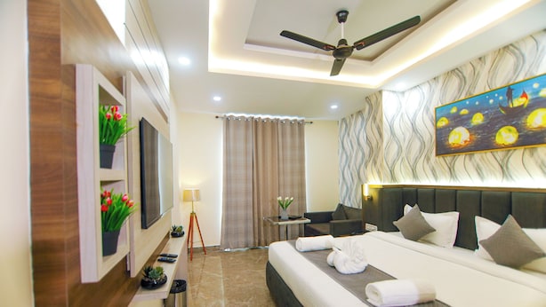 A modern hotel room with a large bed, a ceiling fan, a painting, and a small table with a lamp. - Treebo Paarth Grand (Haridwar)