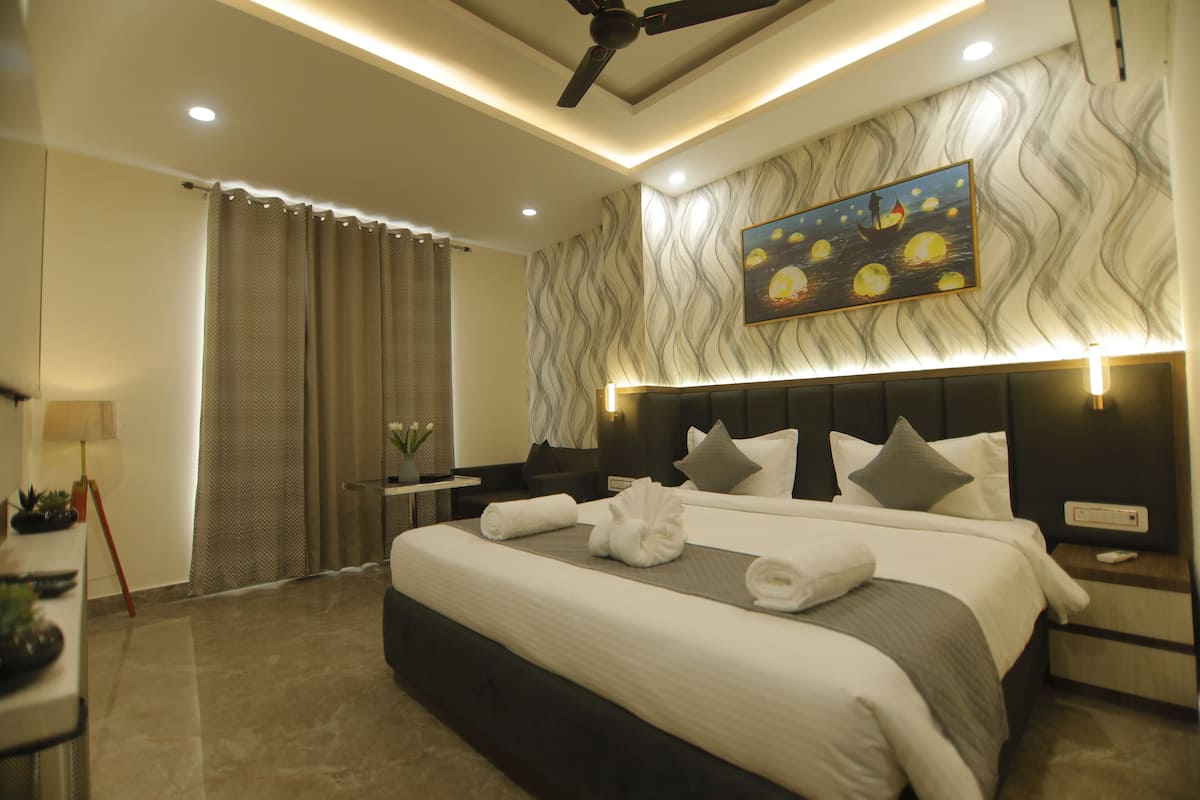 A modern hotel room with a large bed, a ceiling fan, a painting on the wall, and a nightstand with a lamp.