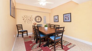 A dining room with a wooden table, six chairs, a clock, and wall art.