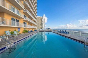 A swimming pool with lounge chairs and a deck, surrounded by a building with balconies.
