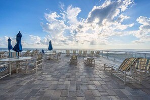 An outdoor terrace with tables and chairs, overlooking a body of water.