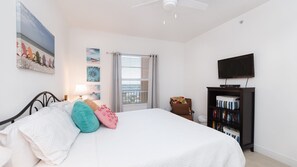 A bedroom with a bed, a TV, a bookshelf, and a window with blinds.