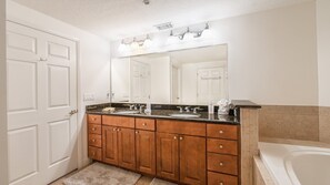 A bathroom with a double vanity, a large mirror, and a bathtub.