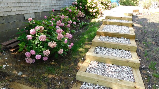 Ein hölzerner Pfad führt zu einem Haus mit rosa Hortensienbüschen.