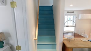 Eine Treppe mit blauen Stufen führt zu einer Empfangsebene mit einer Holztischplatte und einem dreistufigen Metallständer.