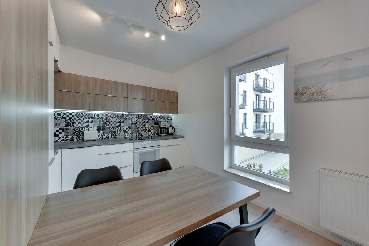 A modern kitchen with patterned backsplash, wooden cabinets, and a dining table with chairs.