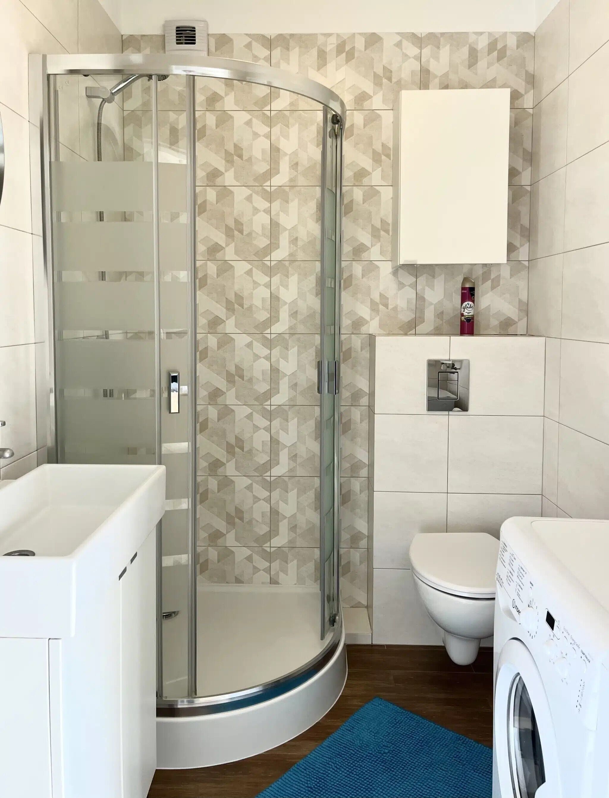 A modern bathroom with a glass-enclosed shower, a white toilet, and a washing machine.