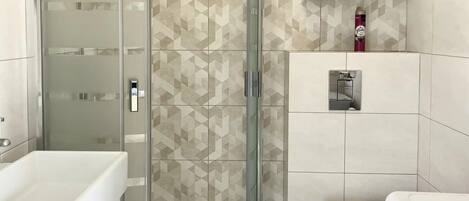 A modern bathroom with a glass-enclosed shower, a white toilet, and a washing machine.