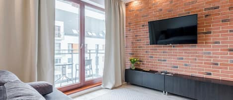 Una sala de estar moderna con pared de ladrillo, televisor de pantalla plana, sofá gris y puerta corrediza de vidrio que da a un área exterior.