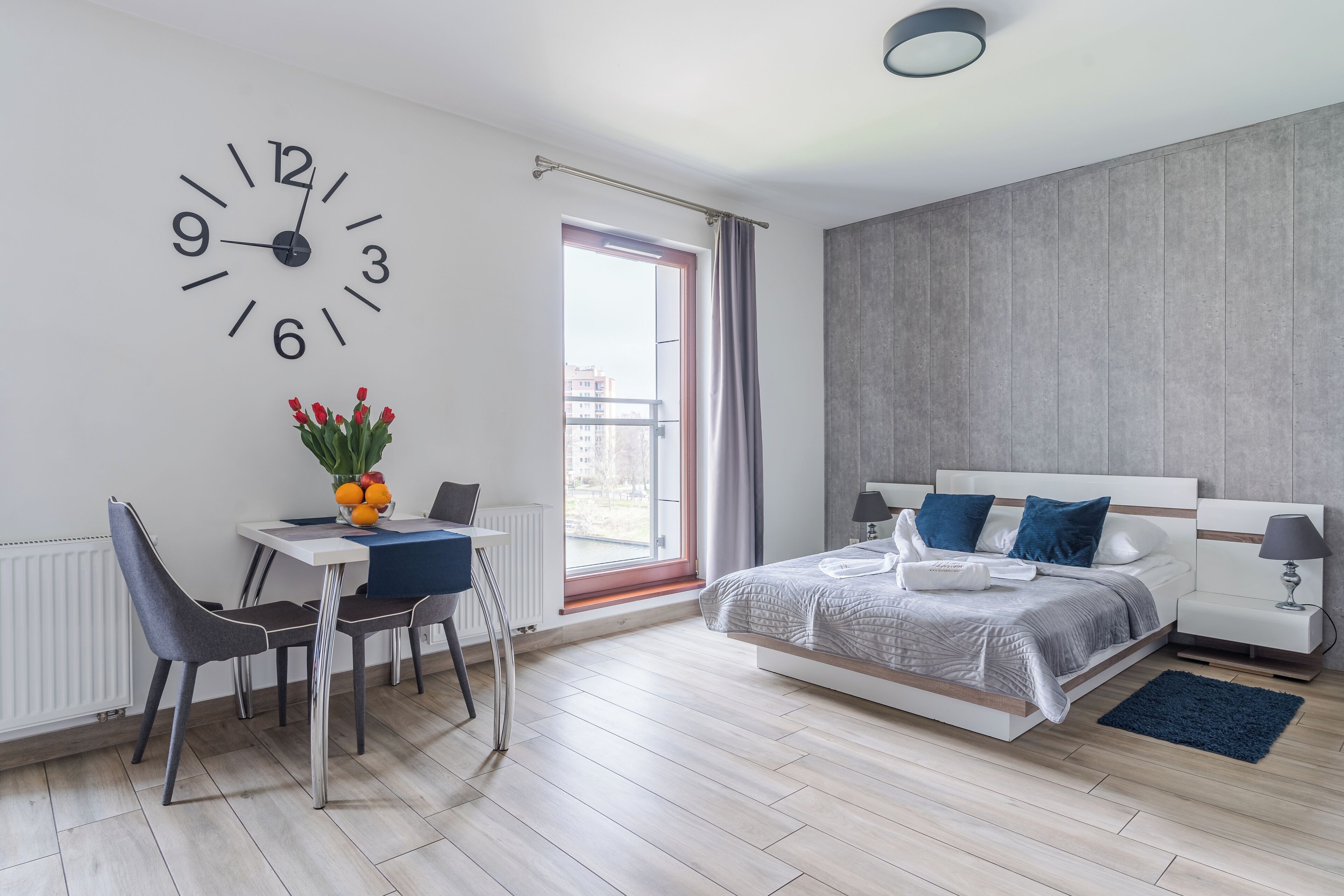 Une chambre à coucher moderne avec un lit, une table de chevet, une lampe et une horloge murale.
